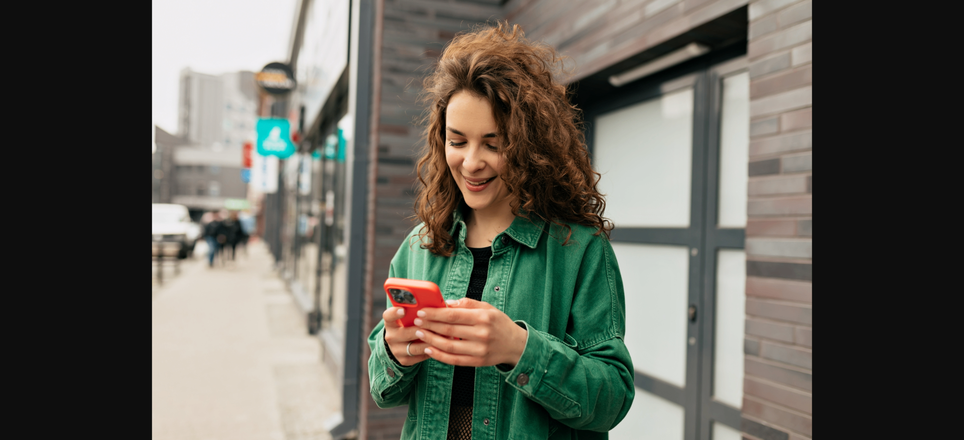 Mulher de cabelos cacheados sorrindo ao usar o celular na rua