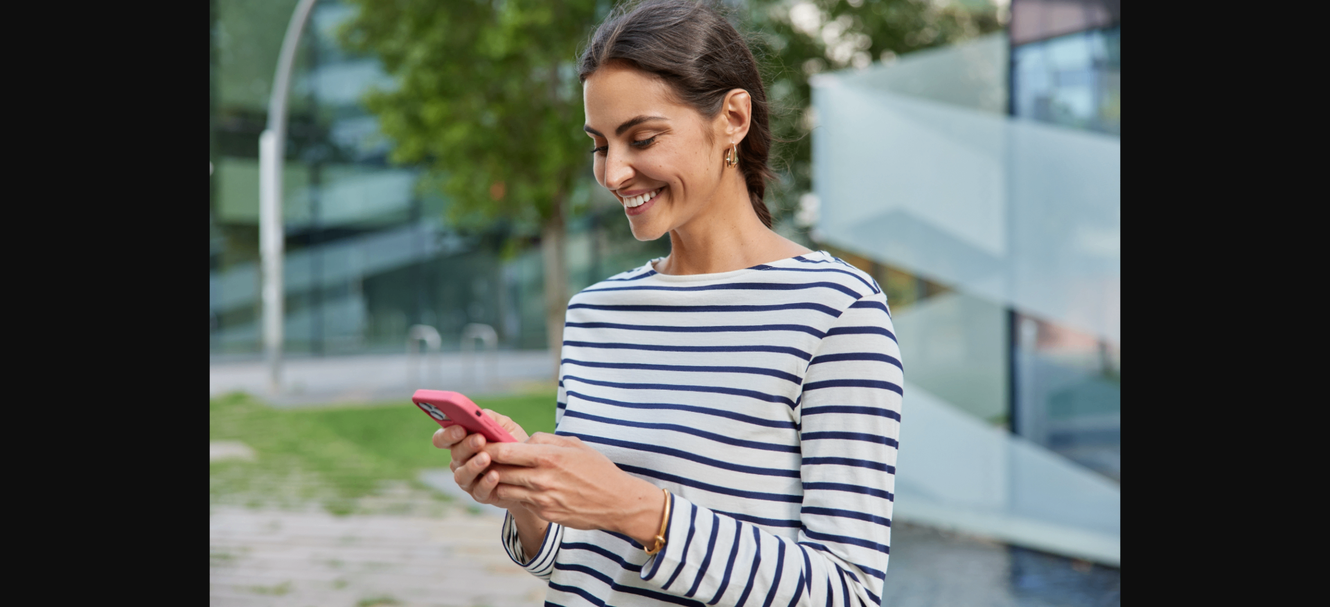 Mulher sorrindo ao usar o celular em frente a um prédio moderno