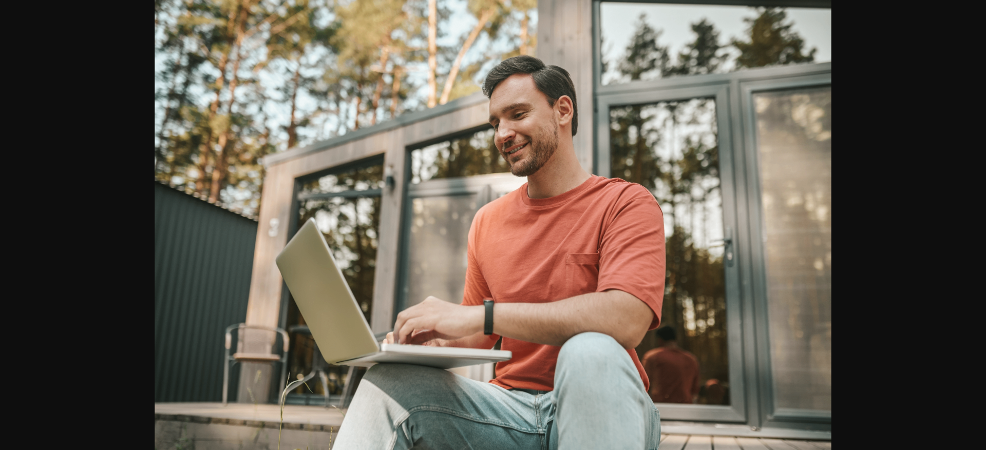 Homem sorrindo ao usar o notebook em uma cabana na floresta